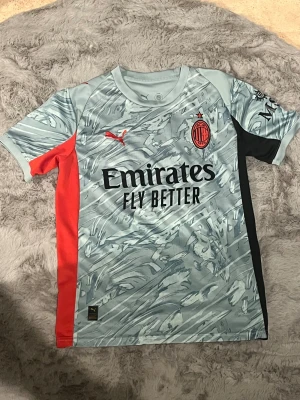 AC Milan bortatröja Puma  - AC Milan bortatröja från Puma i ljusblå med abstrakt mönster, svarta och röda sidopaneler samt klubbmärke och sponsortryck på bröstet. Kortärmad modell i lätt och ventilerande polyester, perfekt för match eller träning.
