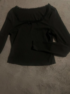 Svart ribbad långärmad topp - Säljer en svart ribbad långärmad, Toppen har en liten rosett framtill och är figurnära i modellen. Perfekt för dig som gillar stilrena och feminina detaljer.
