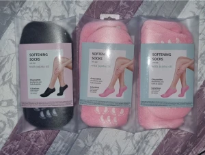 Mjukgörande strumpor med jojobaolja - Tre par mjukgörande strumpor med jojobaolja, två i ljusrosa och ett i svart. Strumporna är korta och har halkskydd under foten. Perfekta för att hålla fötterna mjuka och sköna hemma. Säljs i originalförpackning.