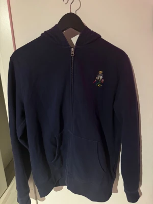 Marinblå hoodie från Polo Ralph Lauren - Marinblå hoodie från Polo Ralph Lauren med dragkedja. Finns qr-kod till hemsida. Används inte, ligger bara och samlar massa damm