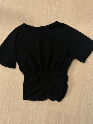 Topp - Säljer en svart topp från Cider i storlek S. Toppen har korta ärmar och en snygg rynkdetalj framtill som ger en cool och modern look. Materialet känns mjukt och skönt mot huden, perfekt att styla med jeans eller kjol för en trendig vibe.