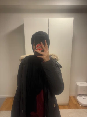 Svart parkas från Woolrich med päls - Svart parkas från Woolrich, modell John Rich & Bros. Jackan har en fluffig beige päls runt huvan, dragkedja och knappar framtill samt två fickor med knappstängning. Perfekt för kalla dagar med sin långa passform och varma material. Den är i ett jättebra skick! Storlek XS. Säljer för 3000 kr.