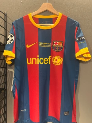 Barcelona Messi 10 Finaltröja 2011 - Barça-matchtröja från Champions League-finalen 2011 med Messi 10 på ryggen. Rödblåa breda ränder, gula detaljer och tryck, officiella FCB-emblem och UNICEF-logga. Kortärmad, rund hals och tillverkad i lätt Dri-Fit polyester. Champions League-patch på ärmen. Helt ny med tagg en replika