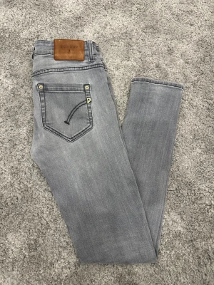 Grå skinny jeans från Dondup - Snygga grå jeans från Dondup med klassisk femficksdesign och guldfärgade detaljer. Jeansen har en smal passform och är tillverkade i mjukt denimtyg. Perfekta för dig som gillar stilrena och moderna jeans med en cool touch.