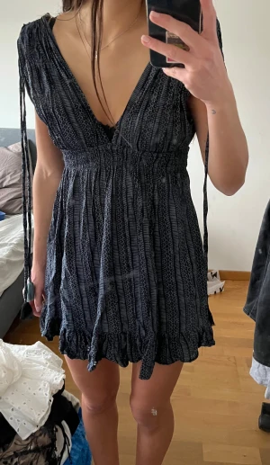 Mörkblå kortklänning med v-ringning - Supersöt mörkblå kortklänning med v-ringad hals och smock i midjan. Klänningen är mönstrad med en  volangkant nedtill och knytband med tofsar vid axlarna. Klänningen är från en liten butik i Thailand och är i storlek onesize, skulle säga att den passar storlek XS-S, jag är 168 cm❤️