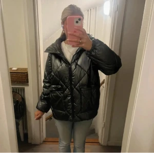 Svart pufferjacka med huva - Säljer en svart pufferjacka med oversized passform och huva. Jackan har quiltad design, dragkedja framtill och stora fickor. Perfekt för kalla dagar och ger en cool, avslappnad vibe till din outfit.