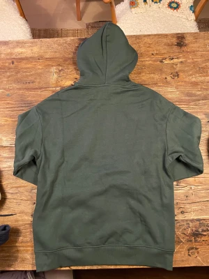 Mörkgrön hoodie från Warp - Snygg mörkgrön snowboard hoodie från Warp med klassisk huva och magficka. Tröjan har ett litet tryck av en snowboard på bröstet och en svart etikett vid nederkanten. Tillverkad i mjuk bomull, perfekt för chill dagar. Passar dig som gillar enkel och clean stil.