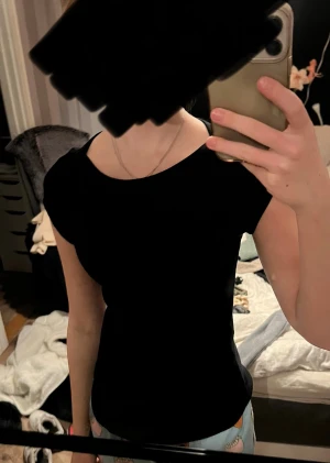 Svart topp från 157, storlek S - En stilren svart topp från 157 i storlek S. Modellen är figurnära med rund hals och korta ärmar. Materialet känns mjukt, ribbat och stretchigt, perfekt för en enkel och clean look. Passar dig som gillar minimalistisk stil och vill ha en basic topp i garderoben.