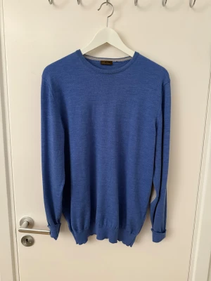 Blå stickad tröja från Stenströms - Snygg blå stickad tröja från Stenströms med rund hals och ribbade muddar. Tröjan har långärmade ärmar och gråa armbågslappar som ger en chill och stilren vibe. Perfekt för dig som gillar klassisk men ändå modern look. Den är utav 100% merino ull och är i utmärkt skick, den ända defekten är ett litet hål vänstra änden av armen som knappt syns (se sista bilden). Storleken är L men den passar också M.