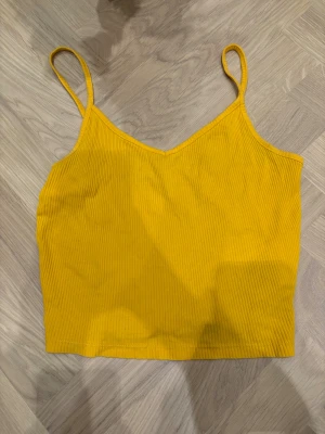 Gul ribbad linnetopp från FB Sister - Snygg gul linnetopp från FB Sister i storlek S. Toppen har smala axelband, v-ringad hals och är ribbad i materialet för en cool struktur. Perfekt att styla med jeans eller shorts när solen skiner. Färgen är riktigt poppig och ger sommarkänsla direkt.