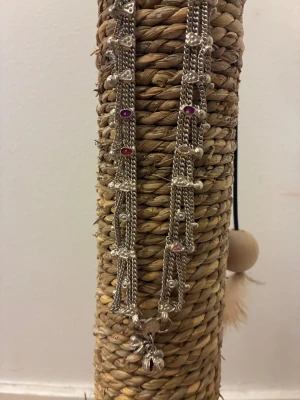 Silvrigt halsband med färgstenar - Unikt silvrigt halsband med flera kedjor, dekorerat med små hjärtan och pärlliknande detaljer. Färgade stenar i lila, rött och rosa ger extra vibe. Nederdelen har hängande berlocker som ger coolt statement. Perfekt för dig som gillar detaljer och vill sticka ut.