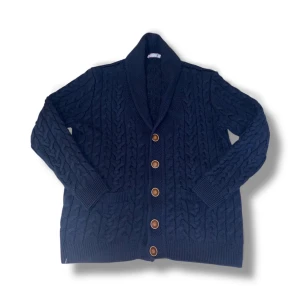 Felix Hardy cardigan  - Säljer en mörkblå stickad kofta med grovt flätmönster och fem bruna knappar framtill. Koftan har bred krage, långa ärmar och ribbade muddar vid ärmslut och nederkant. Perfekt för att hålla sig varm och se chill ut.