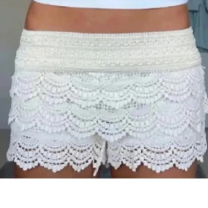 Vita spetsiga shorts med volang - Superfina vita shorts med flera lager volang i spets. De har hög midja och ett romantiskt, boho-inspirerat utseende. Perfekta för varma sommardagar och ger en söt och trendig vibe.