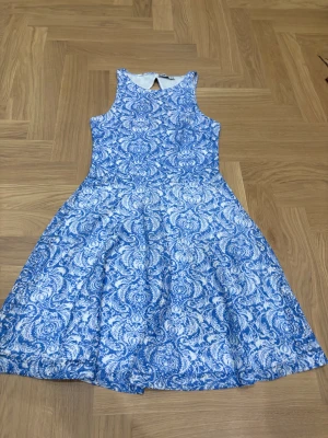Blåvit mönstrad klänning FB Sister - Supersöt blåvit klänning från FB Sister i storlek XS. Klänningen har ett detaljerat paisley-inspirerat mönster, är ärmlös och har en snygg öppen rygg med nyckelhålsdetalj. Modellen är kort med utställd kjol och rund halsringning. Perfekt för dig som gillar färg och mönster.