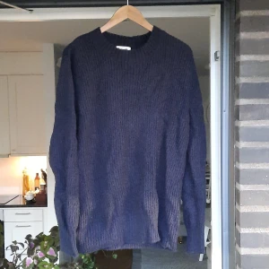 Mörkblå stickad tröja - Säljer en mörkblå stickad tröja med rund hals och ribbade muddar. Tröjan har en enkel, klassisk design och är långärmad. Perfekt för dig som gillar en chill och stilren look under kyliga dagar.