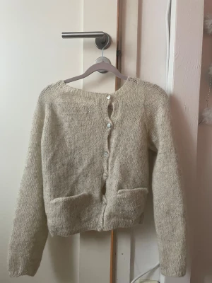 Beige-grå stickad kofta med knappar - Mysig stickad kofta med rund hals och snygga knappar framtill. Koftan har två fickor och är långärmad. Perfekt för lager-på-lager och chill dagar. Materialet är fluffigt och ger en soft vibe. Står inte storlek eller märke, men storleken är som xs/s