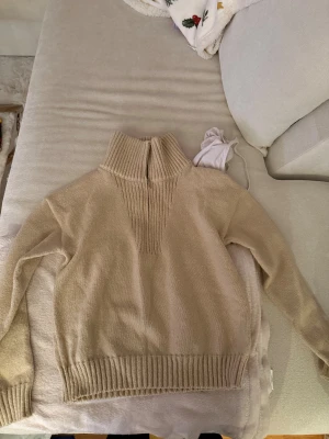 Beige stickad polotröja med half zip - Snygg beige stickad polotröja med ribbad krage och half zip framtill. Tröjan har långa ärmar och breda ribbade muddar vid nederkant och ärmslut. Perfekt för dig som gillar en chill och stilren look.