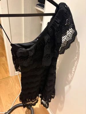 Svart spetsklänning från Dry Lake🖤 - Supersnygg svart kortklänning från Dry Lake med ett axelbandslöst och offshoulder-design. Klänningen har vackra spetsdetaljer och ett omlottliknande fall. Perfekt för dig som vill sticka ut med en elegant och trendig look.