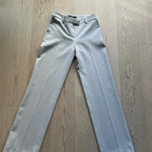 Beiga kostymbyxor från BikBok - Beiga kostymbyxor från BikBok i storlek 34. Byxorna har raka ben, midwaist och klassiska fickor fram. Använd en gång så i mycket bra skick.