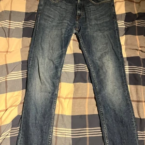 Blå jeans från Tiger of Sweden - Snygga blå jeans från Tiger of Sweden med klassisk femficksdesign och tydliga kontrastsömmar. Jeansen har en rak passform och är tillverkade i slitstarkt denimtyg av bomull. Perfekta för dig som gillar stilrena och tidlösa jeans med diskreta detaljer.