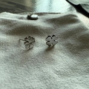 Silvriga fyrklöver örhängen Edblads  - Ett par stilrena örhängen i form av fyrklöver, tillverkade i blankt silverfärgat material. Perfekta att bära för en extra touch av tur och enkel elegans. Små och diskreta studs som passar till alla tillfällen.