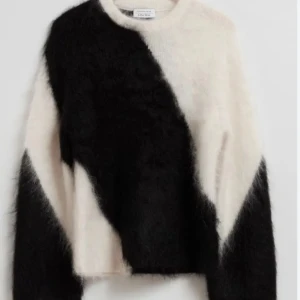 Fluffig svartvit stickad tröja - Säljer en supermjuk och fluffig stickad tröja från Other Stories i svart och vitt. Tröjan har ett coolt, grafiskt mönster och lång ärm. Perfekt för dig som vill sticka ut med en mysig och trendig look.