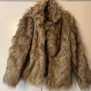Beige pälsjacka från H&M - Säljer en fluffig och oversized beige pälsjacka från H&M. Jackan har lång luddig fuskpäls, bred krage och långa ärmar. Perfekt för dig som vill sticka ut och hålla dig varm under kalla dagar. Stängs med knappar framtill.