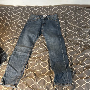 Blå jeans från 157 New Classic W28 L32 - Klassiska blå jeans från 157 New Classic med raka ben och normal passform. Jeansen har fem fickor, orange kontrastsömmar och är tillverkade i slitstarkt denim. Perfekta för dig som gillar en tidlös och enkel stil.