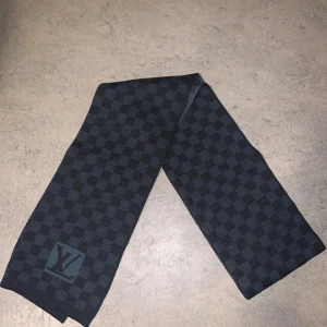  Louis Vuitton damier scarf - Snygg halsduk från Louis Vuitton i mörkblått och svart med klassiskt rutig Damier-design och LV-logga. Halsduken är tillverkad i 100% ull och har en lyxig känsla som lyfter vilken outfit som helst. Möts i Sthlm 