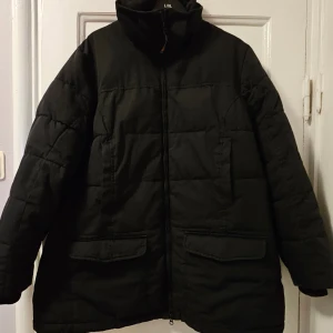 Svart pufferjacka från Lindex XL - Svart pufferjacka från Generous by Lindex i storlek XL. Jackan har hög krage, dragkedja framtill och stora fickor med lock. Quiltad design och långärmad modell, perfekt för kalla dagar. Enkel och stilren look som funkar till det mesta.
