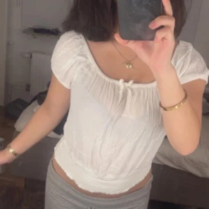 Vit blus från Kappahl med knyt - Supersöt vit blus från Kappahl i luftig bomull. Modellen är croppad med resår i midjan och har korta puffärmar. Söt knytning framtill och lätt rynkad struktur i tyget. Perfekt till sommaren och enkel att styla med jeans eller kjol.