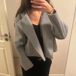 Grå kort kappa från Gina Tricot - Kort, grå kappa från Gina Tricot med dubbelknäppning och stora knappar. Jacka. Har jätte skönt material och använd typ 2 gånger. 