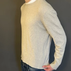 Beige stickad tröja med rund hals - En stilren beige stickad tröja med rund hals och långa ärmar. Tröjan har en enkel design utan mönster eller detaljer, perfekt att matcha med jeans. Materialet känns mjukt och har en lätt ribbad struktur vid muddar och nederkant.