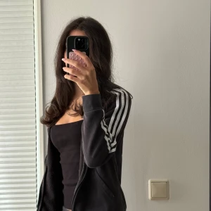 Svart Adidas set, Sweatshirt + Sweatpants - Svart hoodie från Adidas med klassiska vita ränder längs ärmarna och Adidas-logga på bröstet. Tröjan har huva, dragkedja och långa ärmar. Materialet är mjuk bomull och polyester, perfekt för chill eller träning. Snygg och sportig look med normal passform. Snören saknas 💗