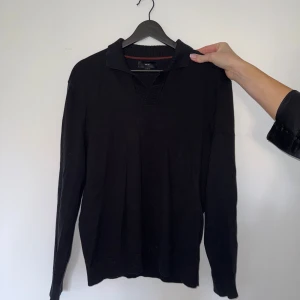 Svart pikétröja från Next i bomull - Svart pikétröja från Next i storlek S. Tröjan har klassisk krage och är långärmad med ribbade muddar. Materialet är mjuk bomull blandat med nylon, vilket gör den skön och lätt att bära. Perfekt för dig som gillar stilrena och enkla plagg.