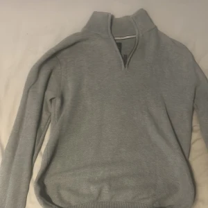 Grå stickad half zip-tröja Bondelid - Snygg grå stickad tröja från Bondelid med half zip-dragkedja och hög krage. Tröjan har lång ärm och ribbade muddar vid ärmslut och nederkant. Perfekt för lager-på-lager och chill stil.