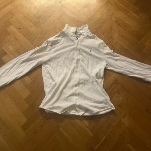 Vit henley från Polo Ralph Lauren S - Vit långärmad henley från Polo Ralph Lauren i bomull. Skjortan har knappar framtill och klassisk broderad logga på bröstet. Perfekt för en clean och stilren look. Snygg passform och mjukt material.
