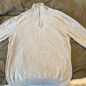 Grå half zip tröja Jack & Jones M - Ljusgrå stickad tröja från Jack & Jones i storlek M. Tröjan har en hög krage med half zip-dragkedja och ribbade muddar vid ärmslut och nederkant. Perfekt för lager-på-lager och chill stil.