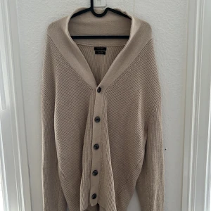 Massimo Dutti Stickad Cardigan - Snygg beige stickad cardigan från Massimo Dutti i extrafin bomull. Koftan har ribbstickad struktur, v-ringning och knäppning framtill med mörka knappar. Perfekt för lager-på-lager och passar till allt. Storlek L, men är lite större i storlek så kan även passa XL. Endast använd en gång. Nypris ligger runt 1699. 🍁Hör av er vid funderingar!🙌🌵