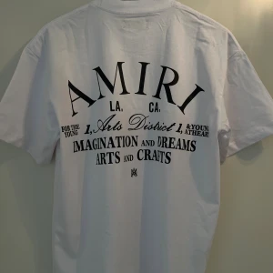 Amiri T-shirt med tryck på baksidan  - Vit t-shirt från Amiri med svart texttryck både fram och bak. Klassisk rund halsringning och korta ärmar. Tillverkad i mjuk bomull för en skön och avslappnad känsla. Snygg streetwear-vibe med tydlig logga och statement-tryck.