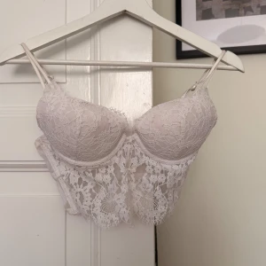 Vit spetbh med tunna axelband - Säljer en vit spetsbh med två tunna justerbara axelband och vacker blommig spets framtill. Toppen har vadderade kupor och hakknäppning i ryggen. Perfekt för dig som vill ha en feminin och trendig look med extra detaljer i spets.