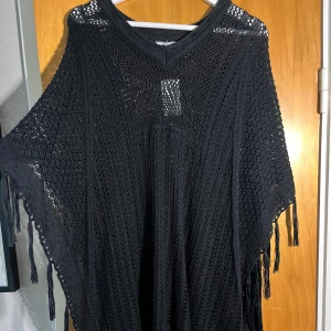 Svart stickad bolerotopp med fransar - Säljer en svart stickad bolerotopp med snyggt hålmönster och v-ringning. Toppen har vida ärmar och fransar längs kanterna för en bohemisk vibe. Perfekt att slänga över ett linne eller bikini. Oversized och luftig modell.