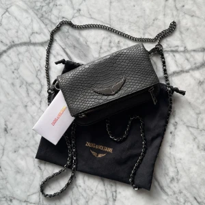 Svart axelväska från Zadig & Voltaire. Nano Soft Savage Rock Clutch - Mörk grå ormmönstrad Zadig väska. I princip helt oanvänd. Jag har även äktightesbevis och dust bagen kvar. Det är den lilla storleken men med många fack. Säljer pga ingen andvändning❤️nypris 3800 kr