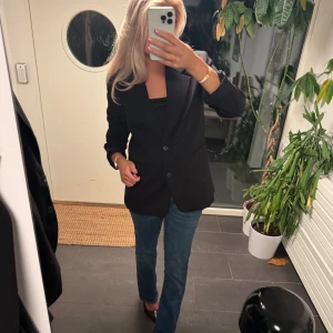 Svart kavaj med klassisk passform - Stilren svart kavaj med två knappar framtill och klassisk krage. Rak och normal passform som ger en snygg siluett. Perfekt att matcha med jeans eller kostymbyxor. Tidlös design utan mönster och med diskreta detaljer.