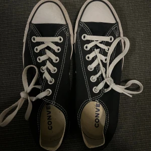 Svarta Converse sneakers låga - Klassiska svarta Converse sneakers med vit tå och sula. Lågt skaft, vita snören och tydliga kontrastsömmar. Ovandel i canvas och rund tå. Perfekta för en avslappnad och cool stil.