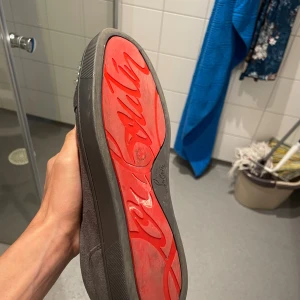 Christian Louboutin sneakers med nitar - Snygga svarta sneakers från Christian Louboutin i mocka med ikonisk röd sula och coola silvriga nitar på tån. Skorna har snörning och en platt sula, perfekt för dig som vill sticka ut med en edgy och lyxig stil.