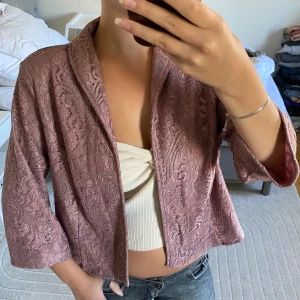 Ljuslila spetsig cardigan jacka - Säljer en ljuslila cardigan jacka med vacker spets och trekvartsärmar. Jackan har en loose passform och är perfekt för dig som vill ha något unikt och stilrent. Den är lätt och har en öppen front utan knappar eller dragkedja.