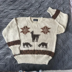 Vintage oversized tröja i 100% ull - Stickad beige Vinted tröja med mönster av lamor. Tröjan är gjord av 50% alpackaull och 50% lamull, har rund hals och långa ärmar med breda muddar. Perfekt för riktigt kalla dagar. Trotts att det står storlek Small så är den oversized och passar mer som M/L. Inga defekt 