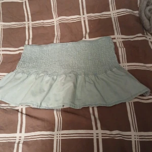 Ljusblå volangkjol från H&M - Supersöt ljusblå kortkjol från H&M med smockad midja och volang nertill. Kjolen har en luftig känsla och är perfekt för varma dagar. Enkel att matcha med både toppar och sneakers för en chill look. L MEN PASSA VERKLIGEN M 