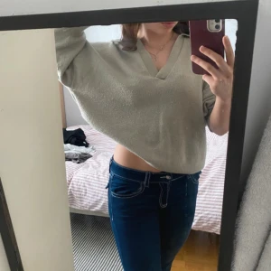 Beige croppad stickad tröja med v-ringning - Säljer en beige croppad stickad tröja med snygg v-ringning. Tröjan har lång ärm och loose passform, perfekt för dig som gillar en avslappnad och trendig stil. Superenkel att matcha med jeans eller kjol för en cool look.